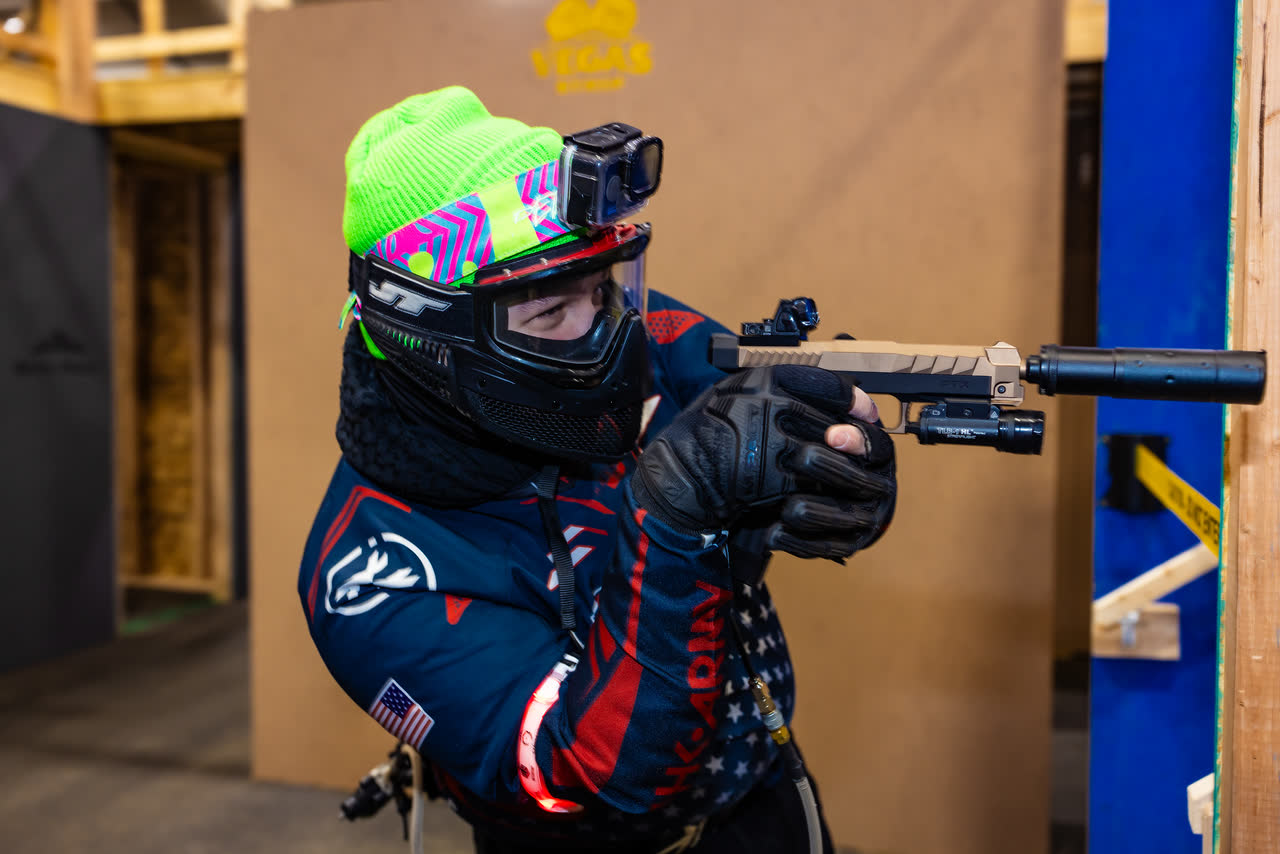 A player aiming a pistol from behind a barricade at an MK Airsoft arena.